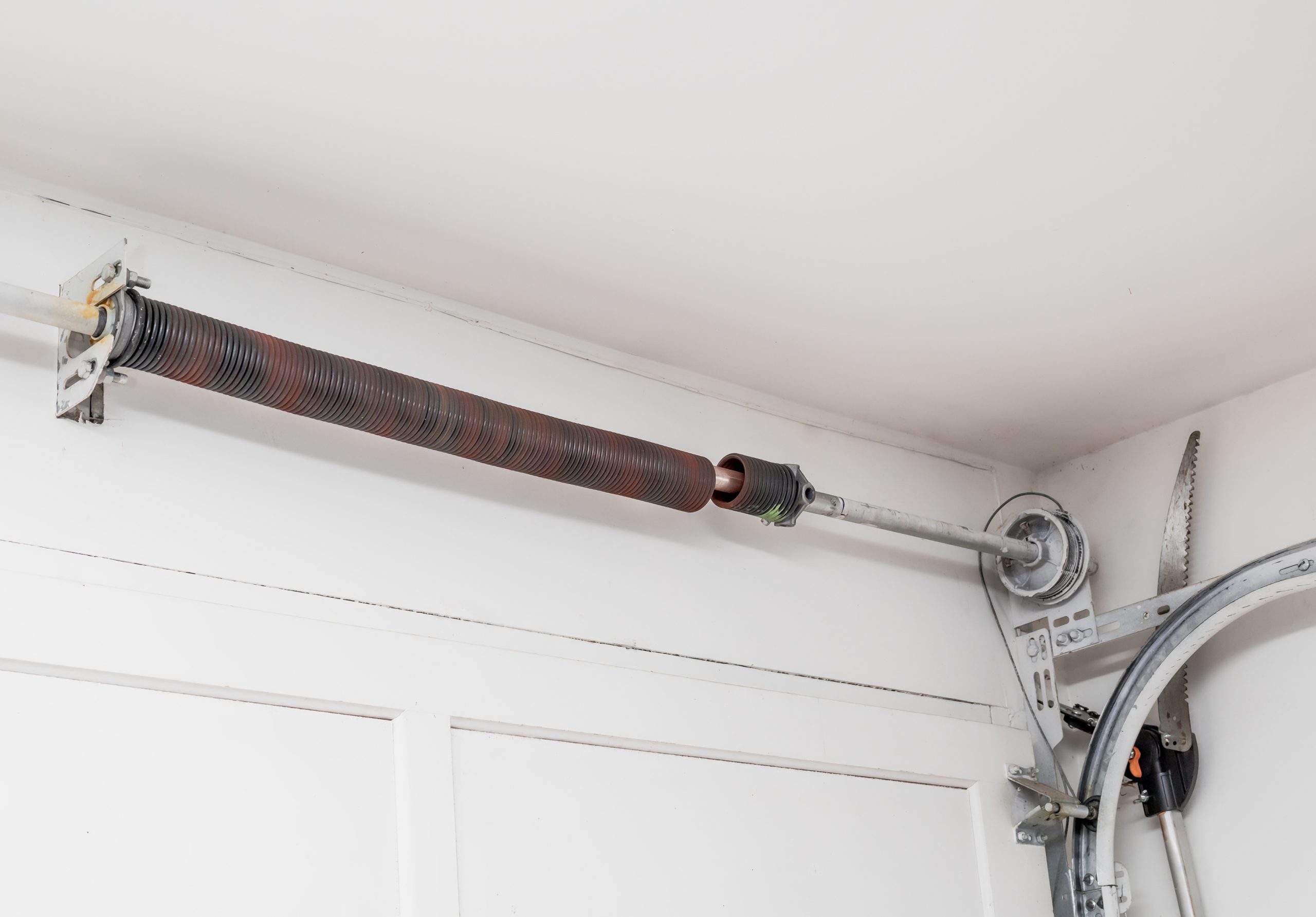 Coiled red-brown flexible conduit mounted to a white wall with metal brackets in a utility/industrial space.