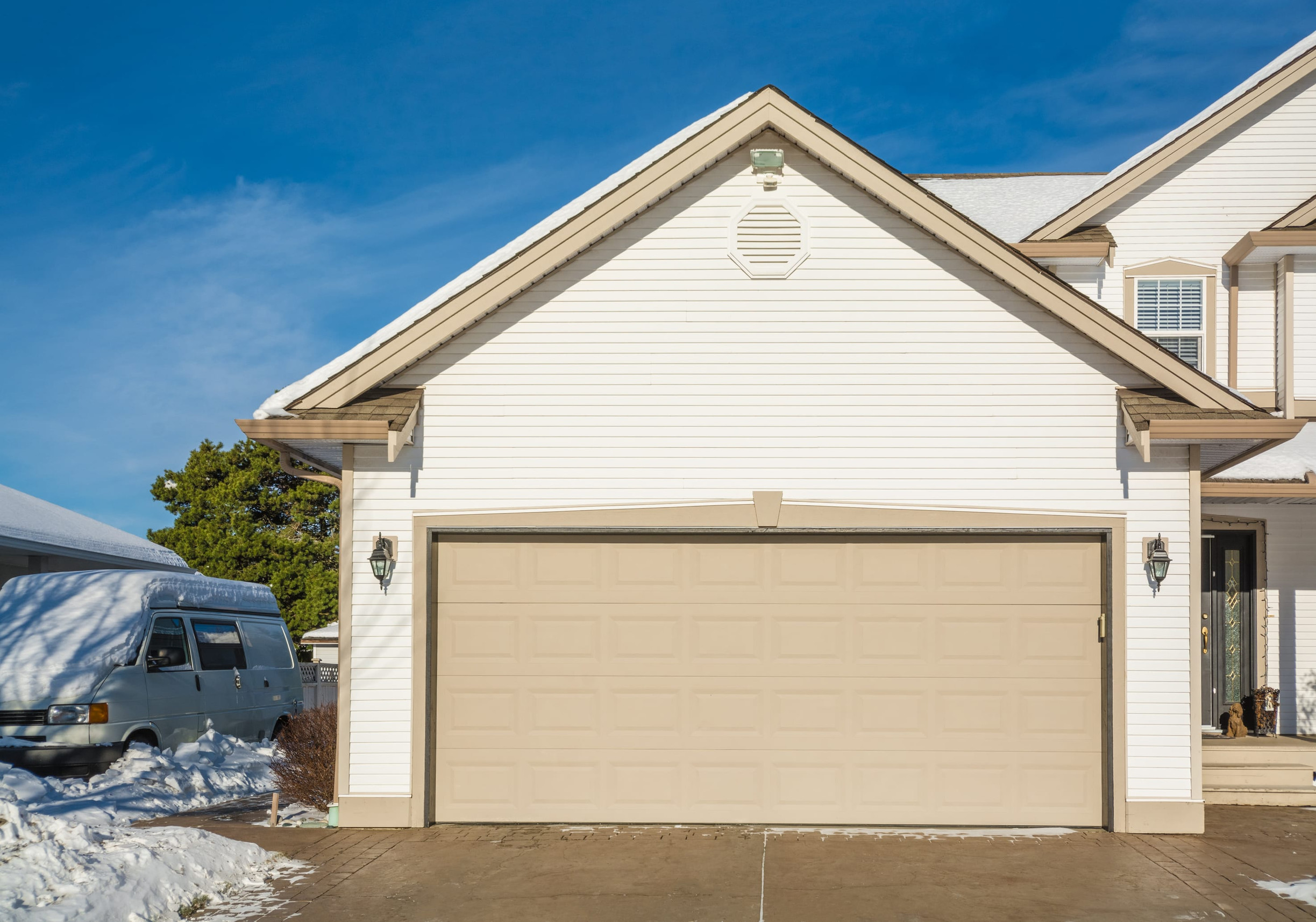 White suburban house with a beige garage door, snow on the ground, and a clear blue sky above.